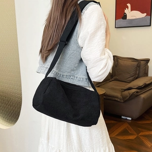 Minimalist black corduroy large capacity crossbody bag shown on a shoulder in a home setting