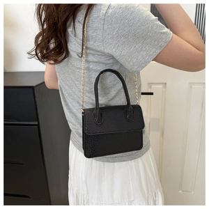 Detail of black lychee grain leather crossbody bag with a slim gold chain strap