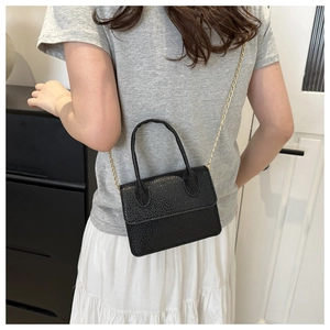 Detail of a black mini square crossbody bag with gold chain strap worn by a model