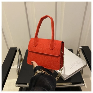 Close-up of orange-red litchi texture leather handbag with gold chain strap detail