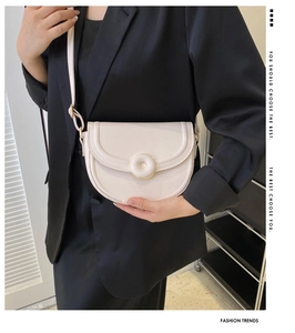 Detail view of cream saddle bag featuring a distinctive gold circular buckle and matte PU leather