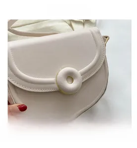 Macro detail of beige saddle bag with round buckle and golden metal trim accents
