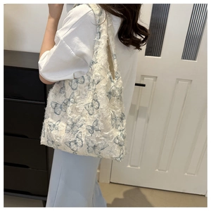 Detail of white jacquard tote bag featuring blue butterfly patterns and fringe trim