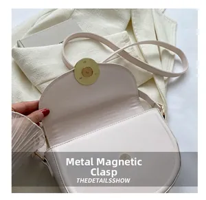 Detail shot of the golden magnetic buckle closure on a cream minimalist saddle bag