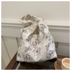 Detail of white jacquard knot bag with black butterfly patterns on wooden table