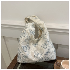 Detail of white jacquard tote bag with blue butterfly patterns and fringe texture