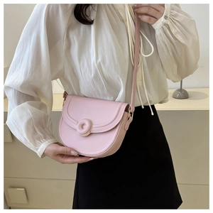 Detail of pink saddle bag featuring a circular magnetic buckle and fine stitching