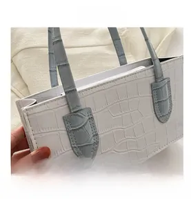 Detail view of white crocodile pattern leather handbag with blue handle and contrast stitching