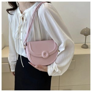 Detail of pink saddle bag featuring a round decorative buckle and adjustable shoulder strap