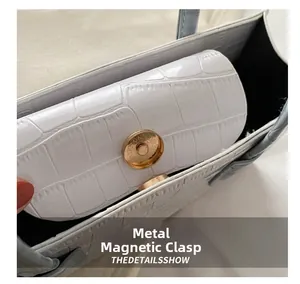 Detailed macro shot of the golden magnetic closure on a white crocodile pattern handbag