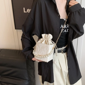 White bucket bag with pearl handle and gold chain strap worn by a fashion model