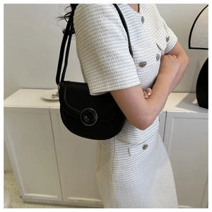 Side view of black leather saddle bag with gold-trimmed round buckle on white tweed outfit