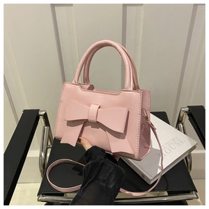 Detail of pink crossbody bag with large bow decoration and golden metal buckle on leather seat