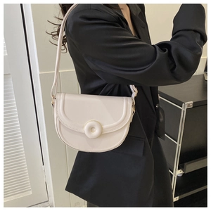 Detail of a minimalist cream-colored saddle bag with metallic circular buckle decoration