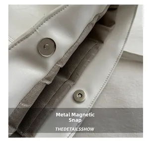 Detail of silver magnetic snap closure and herringbone lining inside a white tote bag
