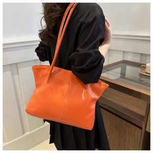 Close-up of vibrant orange glossy tote bag with sleek shoulder strap and seam details