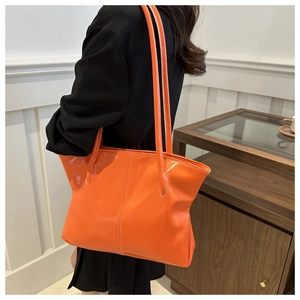 Detail of vibrant orange tote bag in glossy synthetic leather with shoulder straps