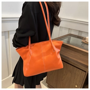 Close-up of bright orange PU tote bag with white contrast stitching on model side