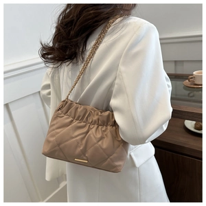 Quilted khaki chain shoulder bag with metal strap detail shown on a female model