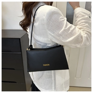 Détail du sac sous le bras en cuir noir avec lettrage FASHION doré porté par un mannequin