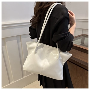 Detail of a white glossy tote bag with slender straps worn on the shoulder by a model