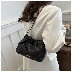 Detail of black quilted shoulder bag with chain strap shown on model in a stylish setting