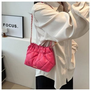 Close-up of pink quilted crossbody bag with gold chain strap worn on cream shirt