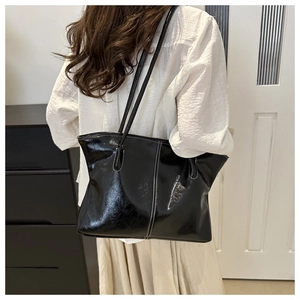 Detail view of large black patent leather tote bag with white stitching and long handles