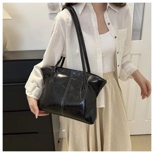 Detail view of large black glossy tote bag with white contrast stitching and slim handles