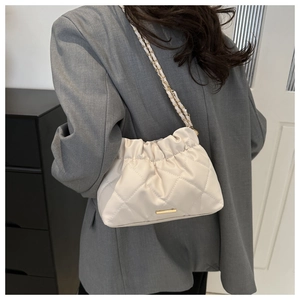 Close-up of beige quilted crossbody bag with gold chain strap worn on grey blazer