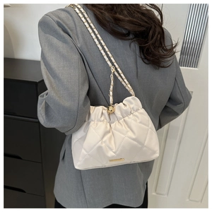 Detail of cream quilted shoulder bag featuring gold chain strap and elegant ruching