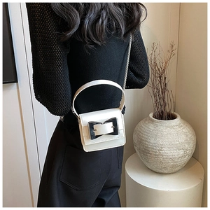Close-up of white mini handbag featuring a bold silver buckle and metal chain strap