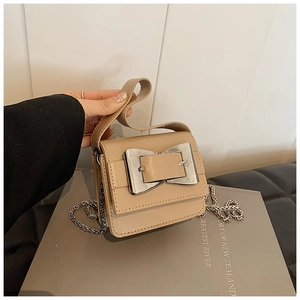 Detail view of mini beige crossbody bag with silver bow buckle and metal chain strap