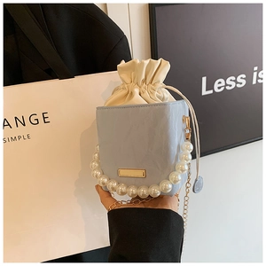 Detail of light blue pleated bucket bag featuring pearl handle and gold chain strap
