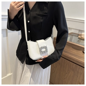 Detail shot of a white leather crossbody bag with a sparkling crystal buckle on model