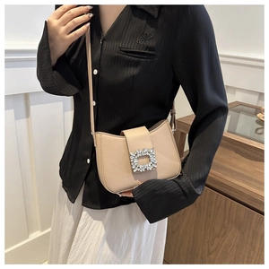 Close-up of cream crossbody bag with rhinestone buckle worn by a model on black shirt