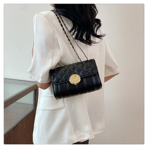 Detail of classic black quilted shoulder bag with gold chain strap worn by a model