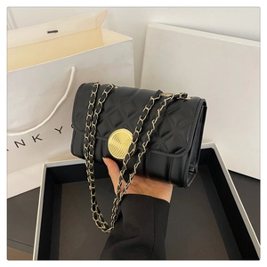 Close-up of black quilted shoulder bag with gold chain strap and luxury gift packaging