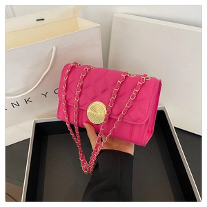 Detail of rose red quilted mini bag with golden clasp and chain strap held by hand