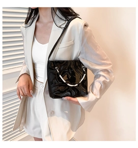 Detail view of black glossy marble textured underarm bag with white pearl chain strap