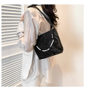 Detail of black underarm bag featuring glossy wrinkled texture and pearl beaded chain strap