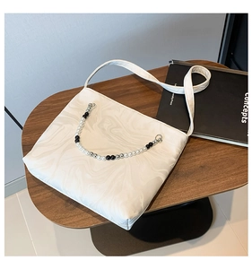 Detail of white marble textured shoulder bag with decorative beaded chain on a wooden table