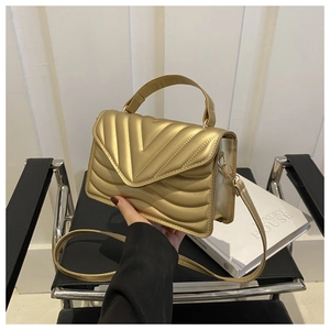 Detail van gouden crossbodytas met V-vormig stiksel en glad handvat bovenaan