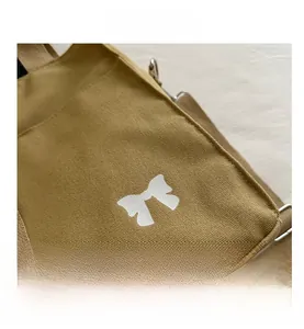 Close-up of canvas tote bag featuring white bow graphic and silver metal swivel hooks