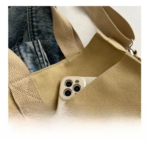 Detail shot of the canvas tote bag showing the exterior pocket with a smartphone inside
