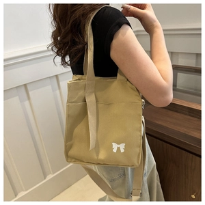 Detail of canvas bag featuring wide shoulder strap and artistic white bow print