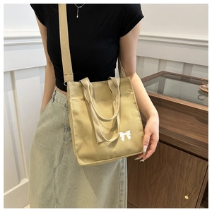 Detail of minimalist khaki canvas tote bag with white bow print worn as a crossbody bag