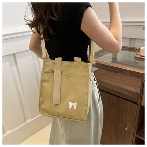 Khaki canvas tote bag with white bow print shown on a model in a cozy indoor setting