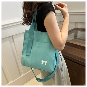 Detail of mint green canvas tote bag featuring a white bow print and adjustable strap
