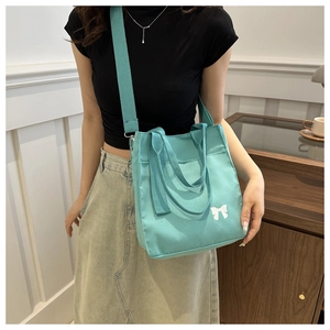 Detail of mint green canvas tote bag with white bow accent and wide shoulder strap
